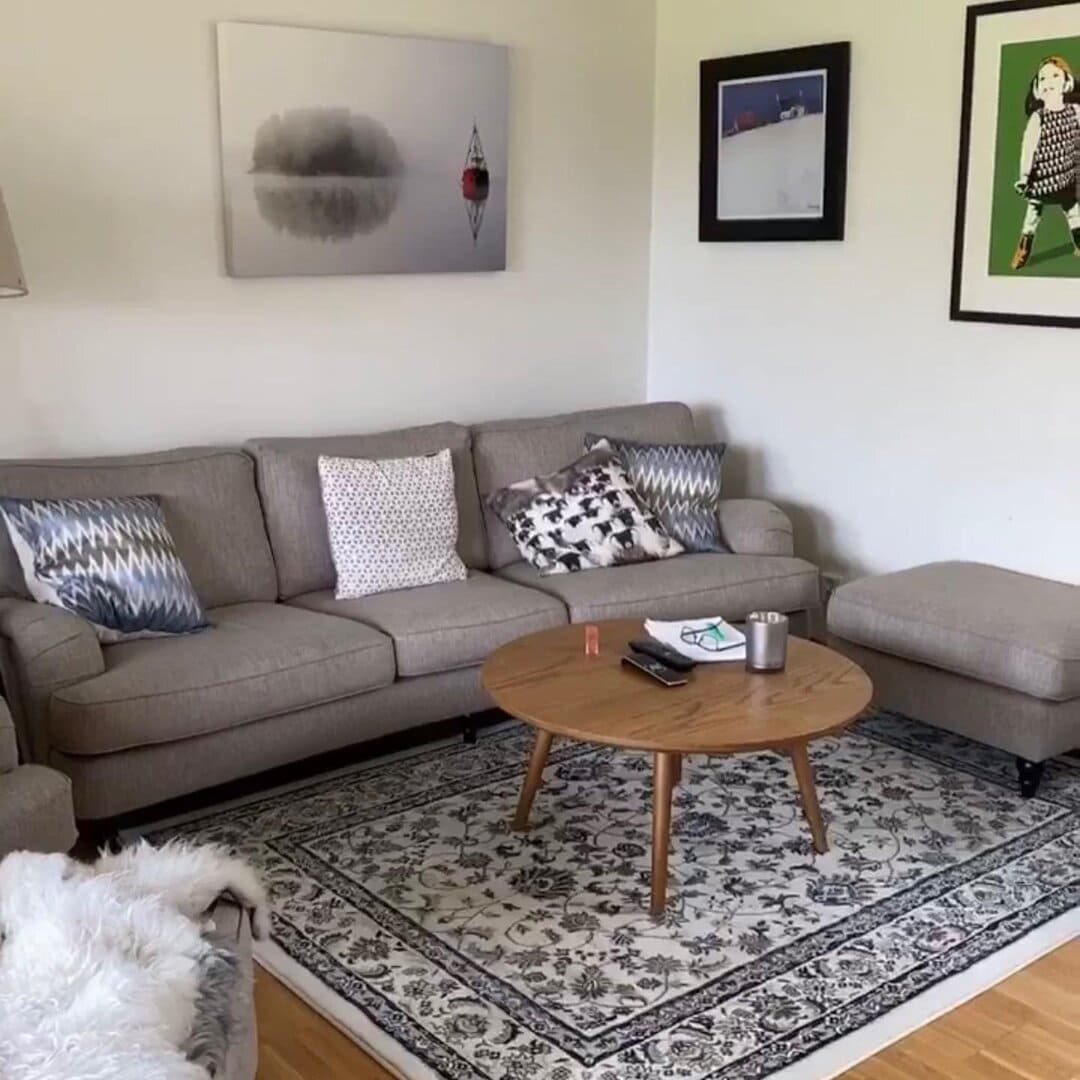 Moderne stue med komfortabel grå sofa, kunstverk på veggen, og et rundt trebord på et elegant teppe, perfekt for avslapning og hjemmetrening.